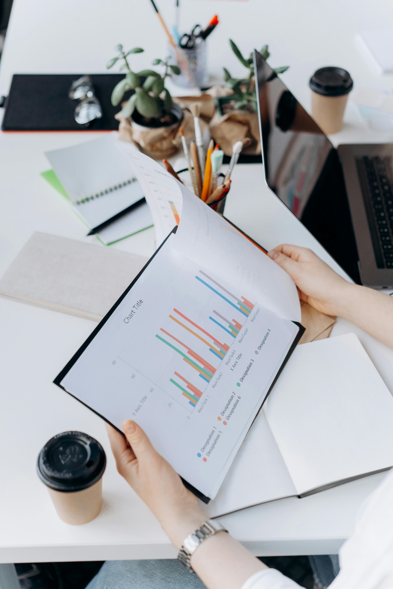 Hands holding a printed chart report on a desk with laptop and notebooks